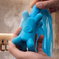 Hand holding the Fähloo silicone handle in the shower with the blue mesh hanging below
