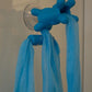Blue Fähloo mesh and handles hanging from the clear Fähloo Shower Valet on a shower wall