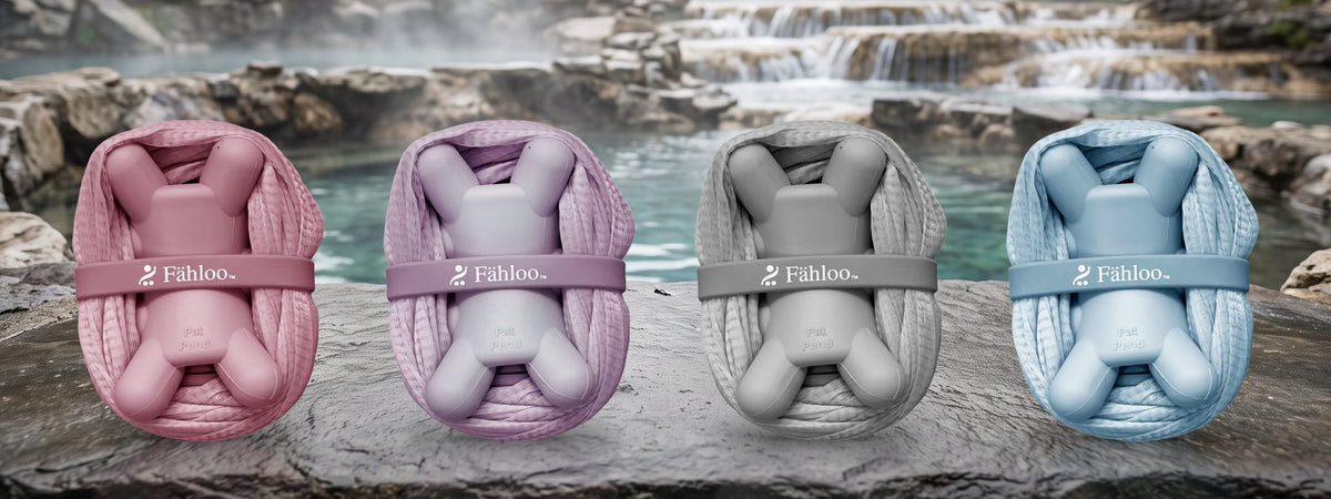 Four Fähloo exfoliating bathing meshes, bundled, in Desert Rose, French Lilac, Pebble Grey and Sea Salt Blue on a stone ledge by a hot spring
